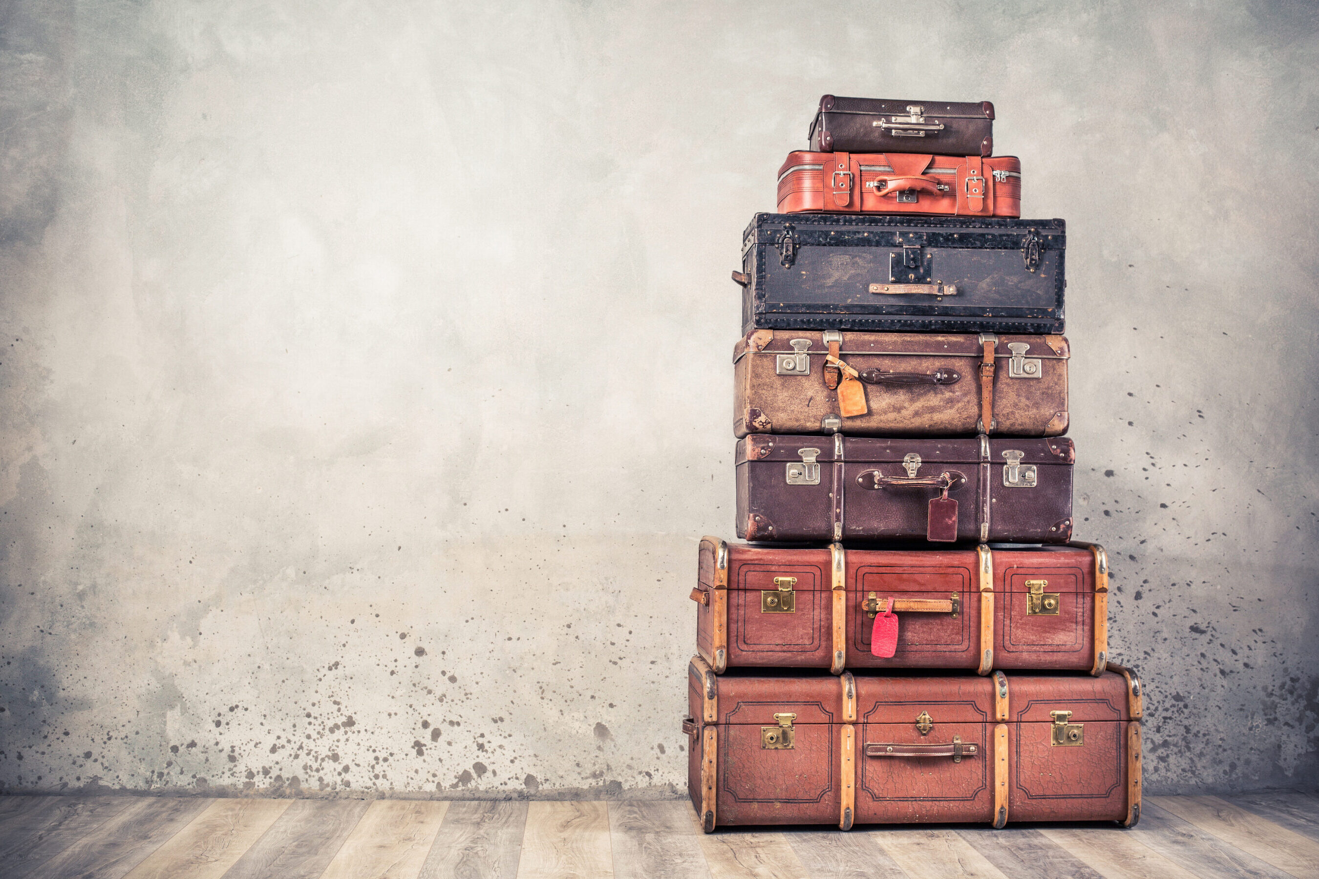 Vintage classic outdated trunks luggage with tags, old antique leather suitcases tower front concrete wall background. Travel baggage concept. Retro style filtered photo